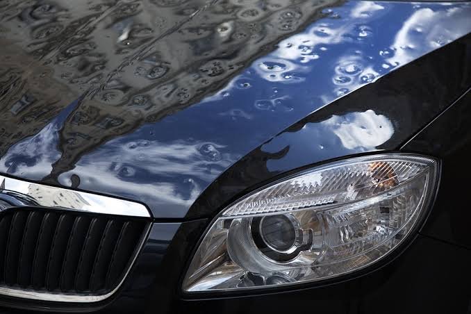 Close-up of a black car hood heavily dented after a hailstorm, showing severe metal indentations that require Paintless Repair Hail Damage.