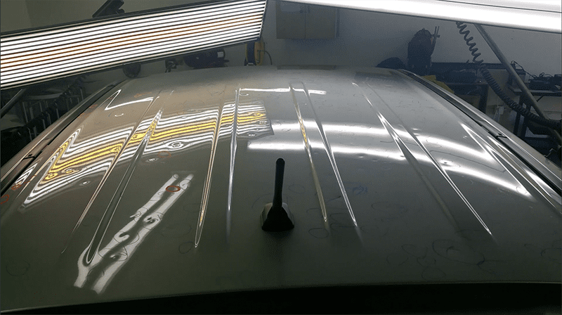 An LED reflection board illuminates marked dents on a car roof during a Paintless Repair Hail Damage inspection.
